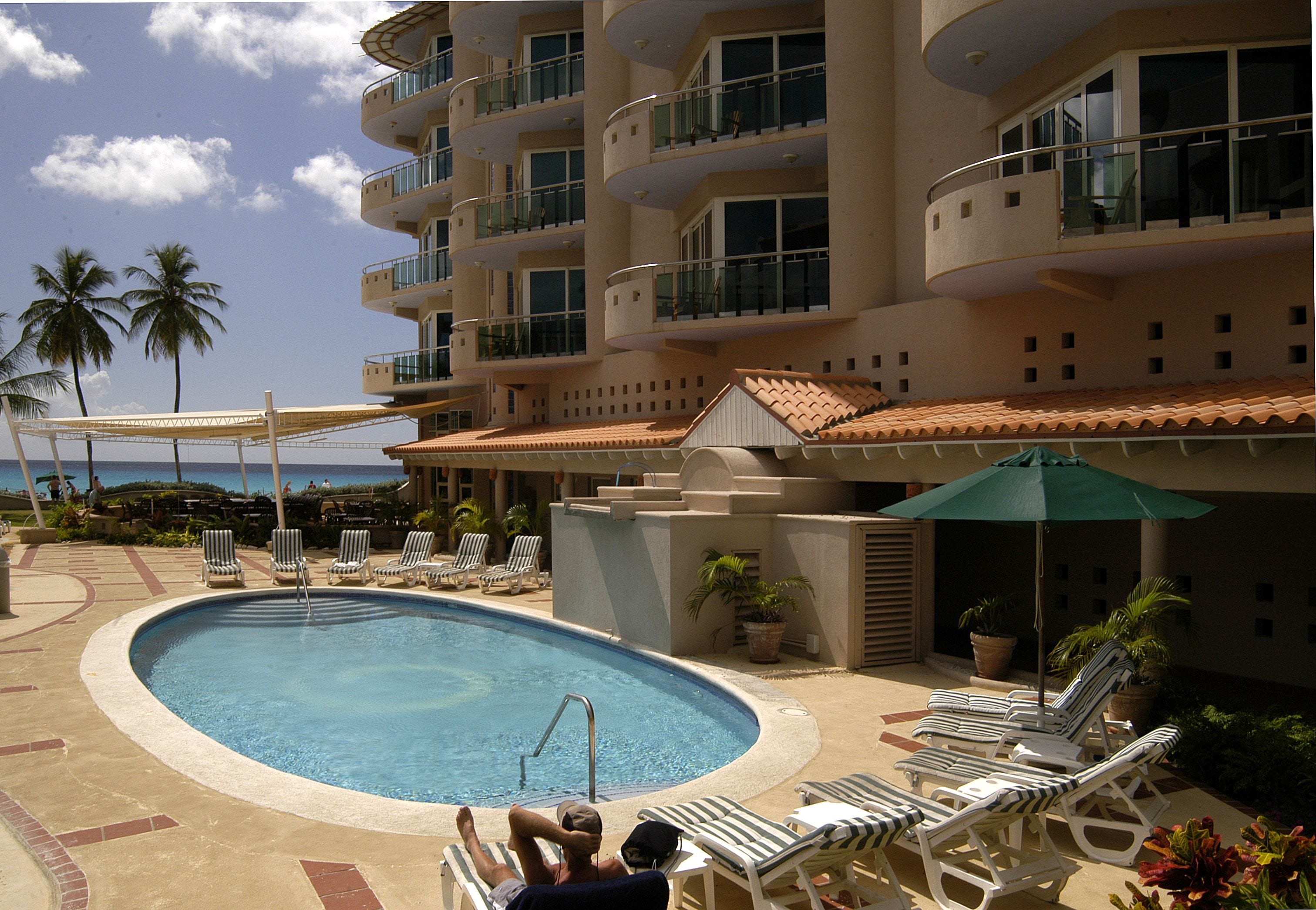 A swimming pool with lounge chairs and umbrellas, surrounded by a multi-story building with balconies.