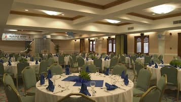 A banquet hall with round tables set for a formal event, featuring green upholstered chairs and white tablecloths.