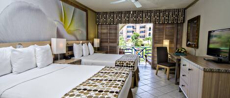 A hotel room with two beds, a desk, a TV, and a balcony with a view of buildings.