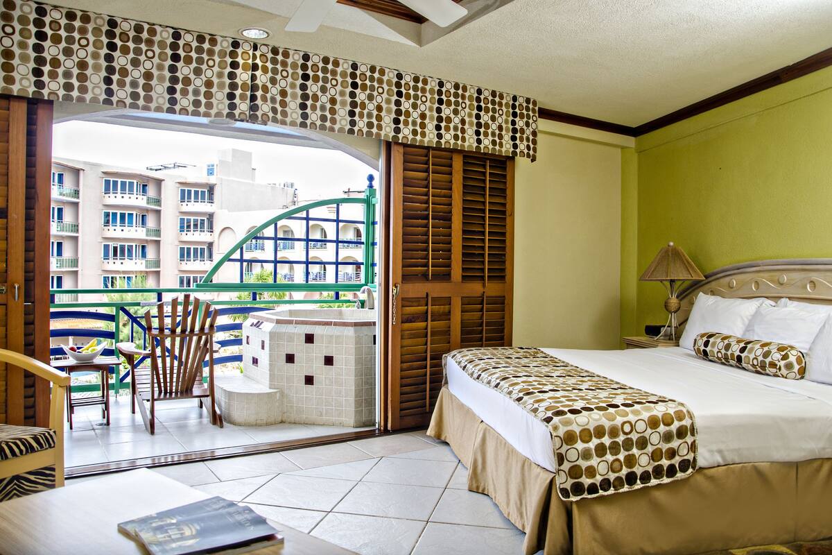 Ein Hotelzimmer mit Bett, Stuhl, kleinem Tisch und Blick auf ein Gebäude durch eine Glastür.