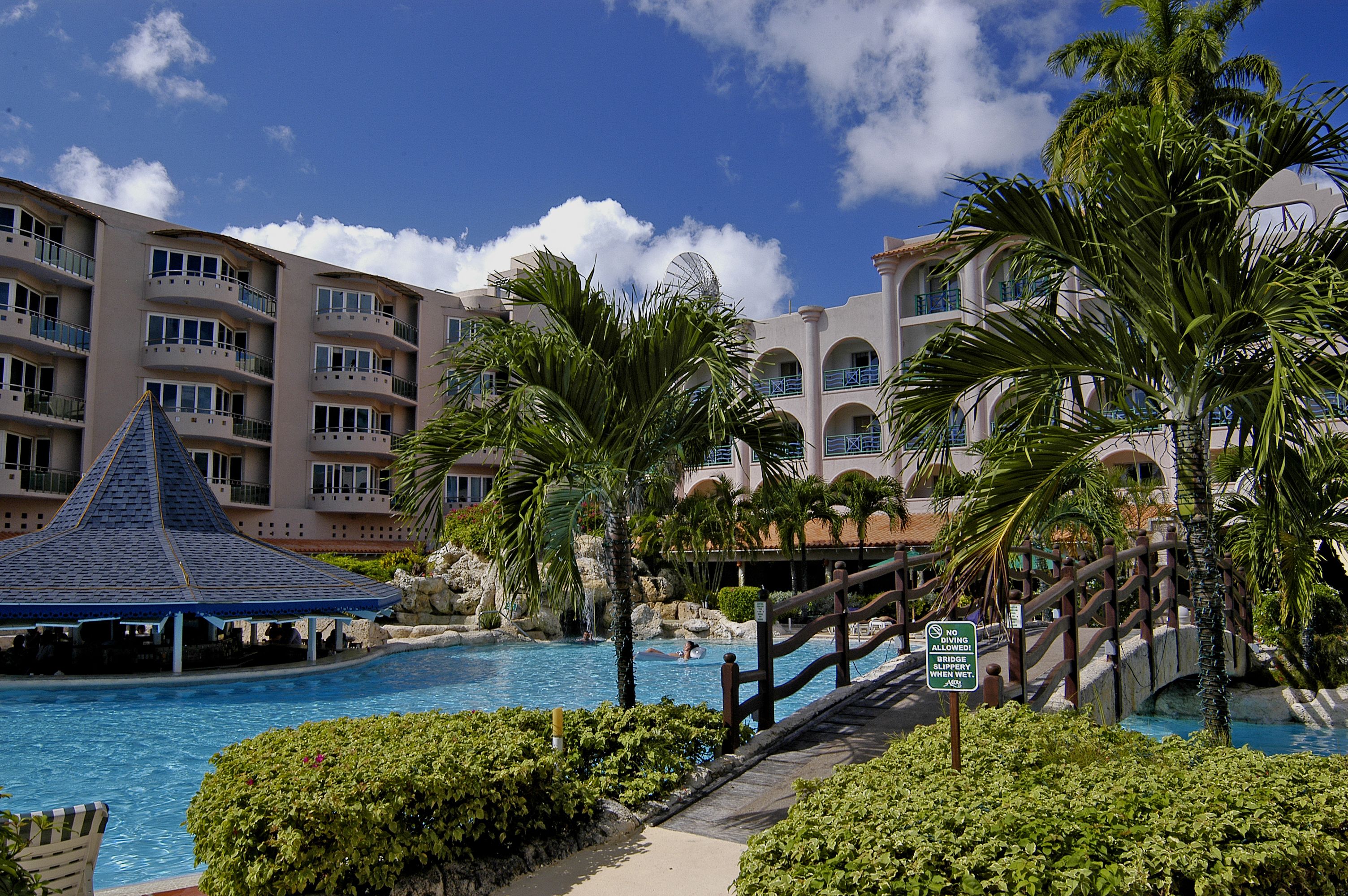 A resort with a swimming pool, palm trees, and a multi-story building with balconies.