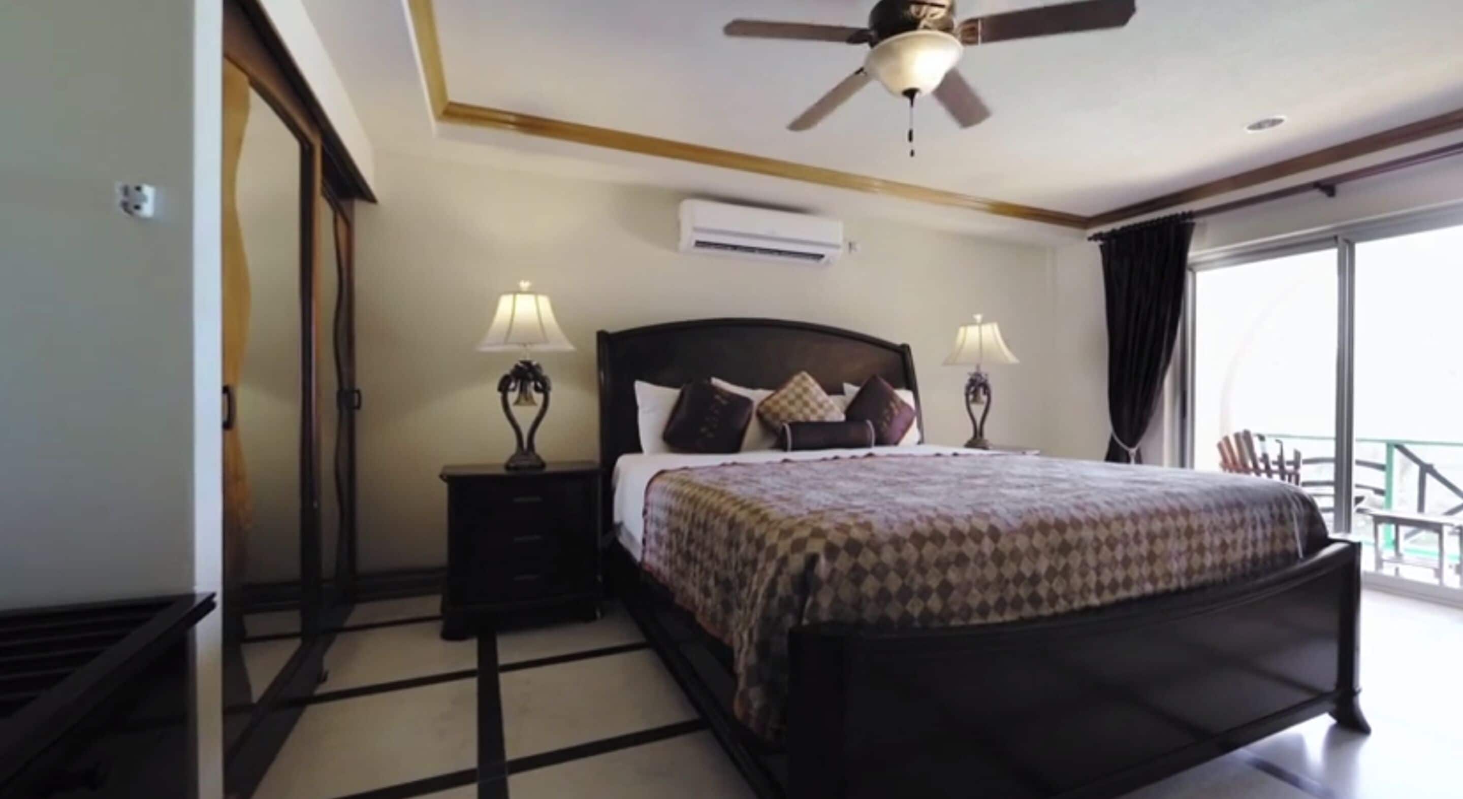Hotelkamer met een bed, twee bedlampen, een plafondventilator, een airconditioner en uitzicht op het balkon.