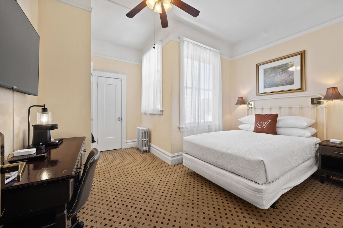 A hotel room with a bed, desk, chair, and a ceiling fan.