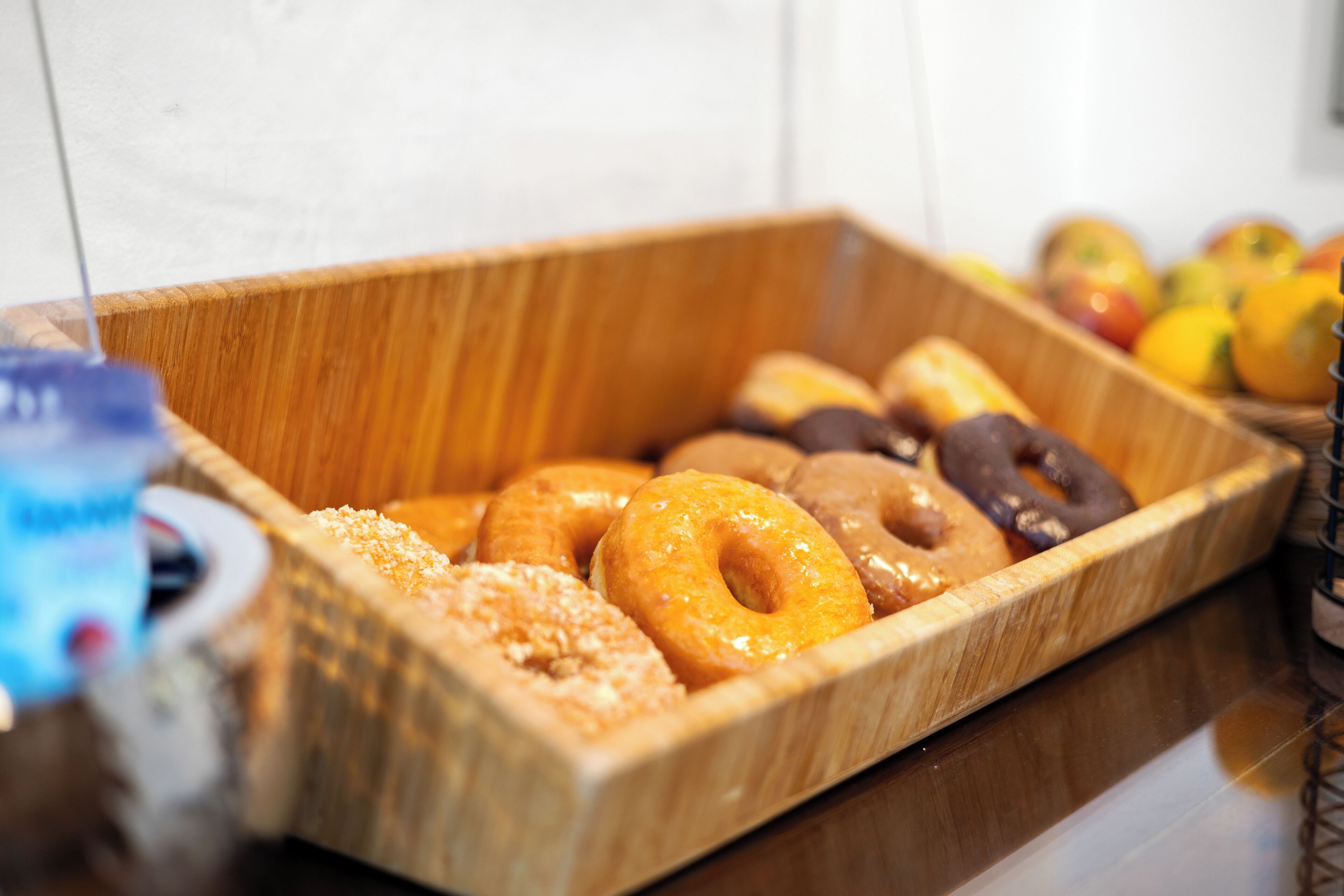 A wooden tray containing various donuts and a bottle of syrup.