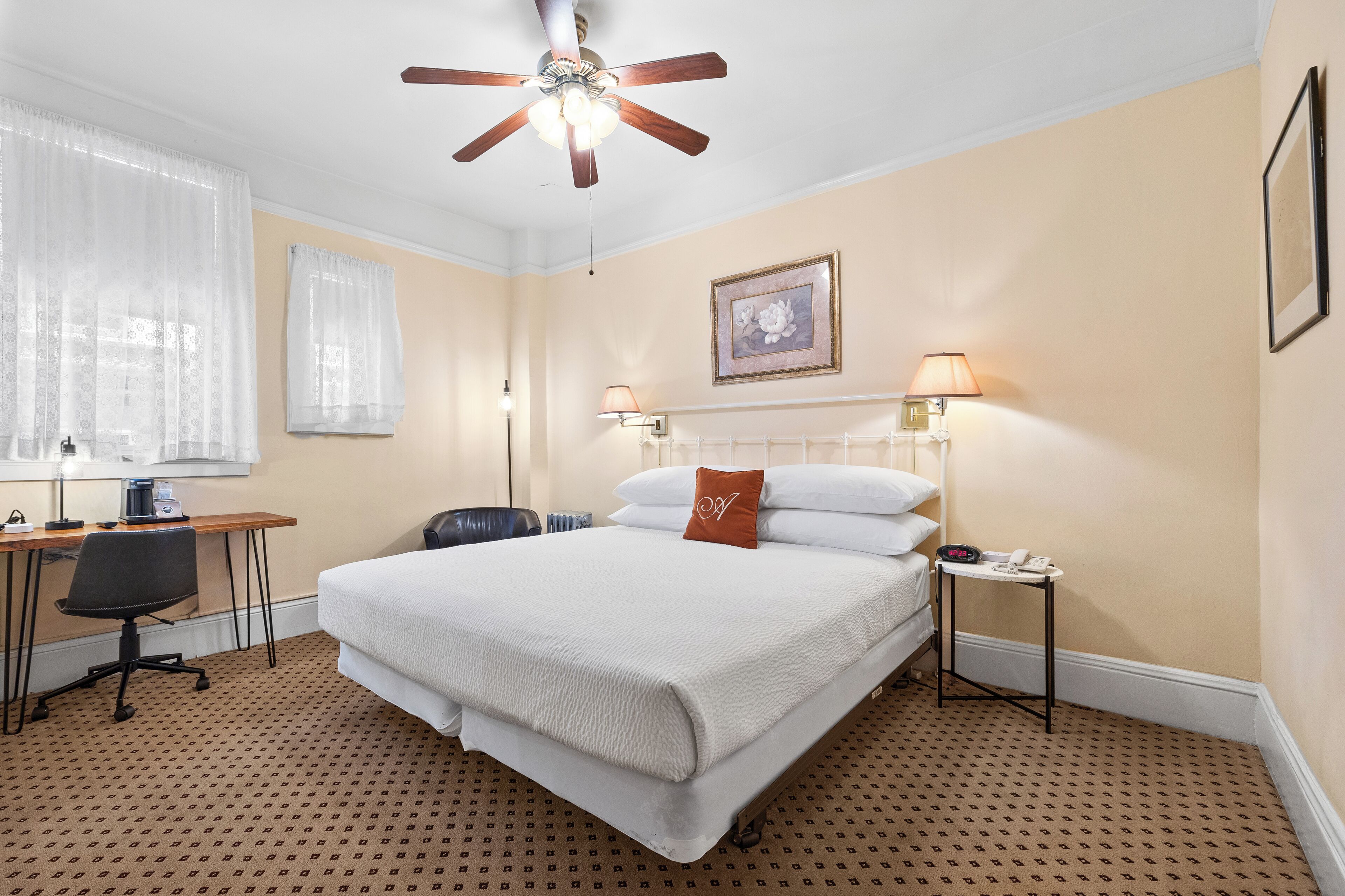 Une chambre d’hôtel équipée d’un lit, d’un bureau, d’une chaise, d’un ventilateur de plafond et de lampes de chevet.
