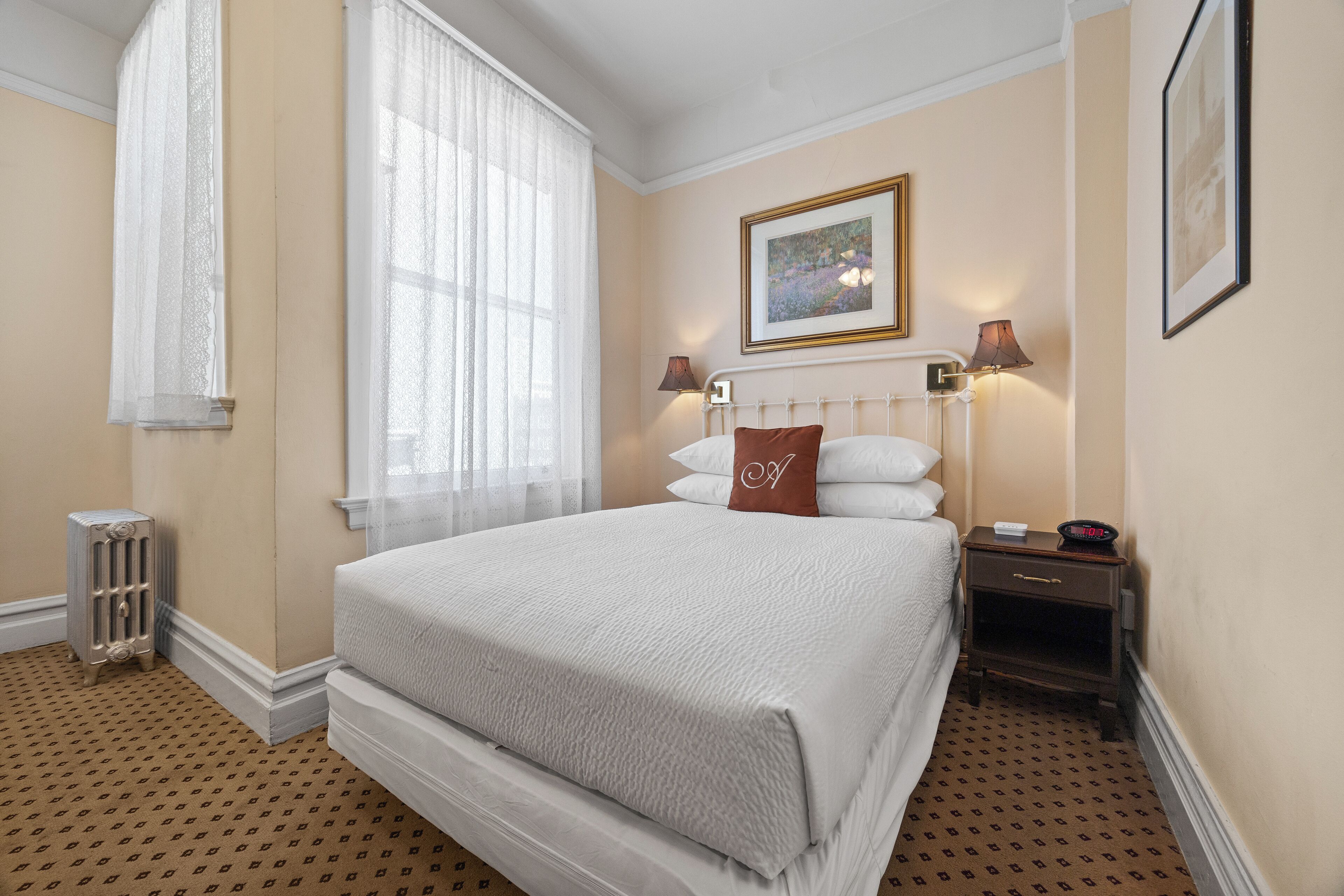 A hotel room with a large bed, two bedside lamps, a radiator, and a framed picture on the wall.