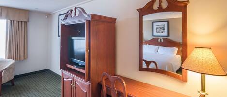 Een hotelkamer met een houten bureau, een televisie, een spiegel, een lamp en een bed.