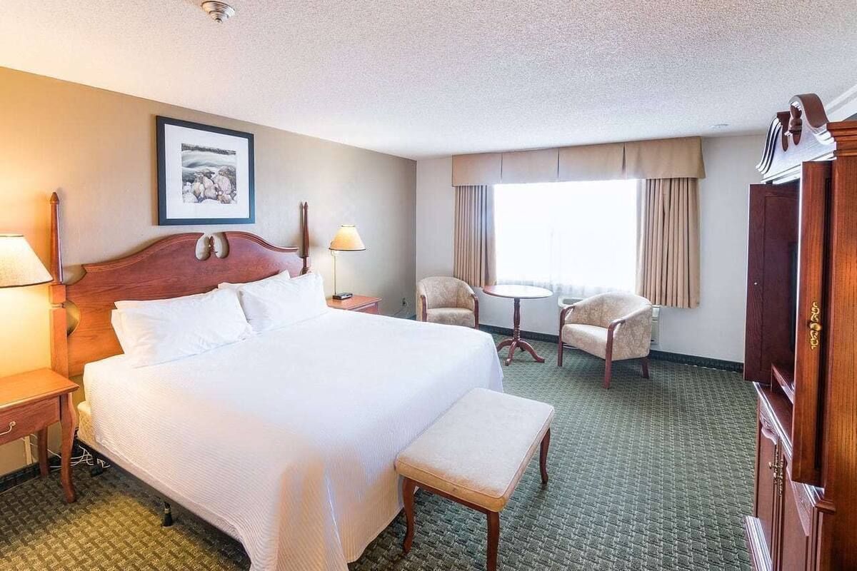 A hotel room with a large bed, two chairs, a small table, a desk, and a wardrobe.