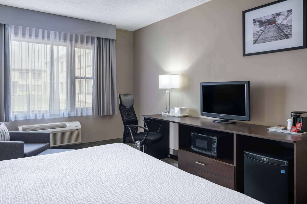 A hotel room with a bed, a desk with a computer, a TV, a microwave, and a small refrigerator.