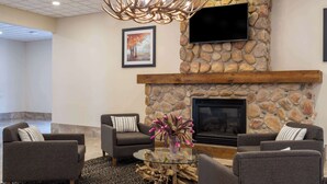 A modern living room with a stone fireplace, comfortable seating, and a large flat-screen TV mounted on the wall.