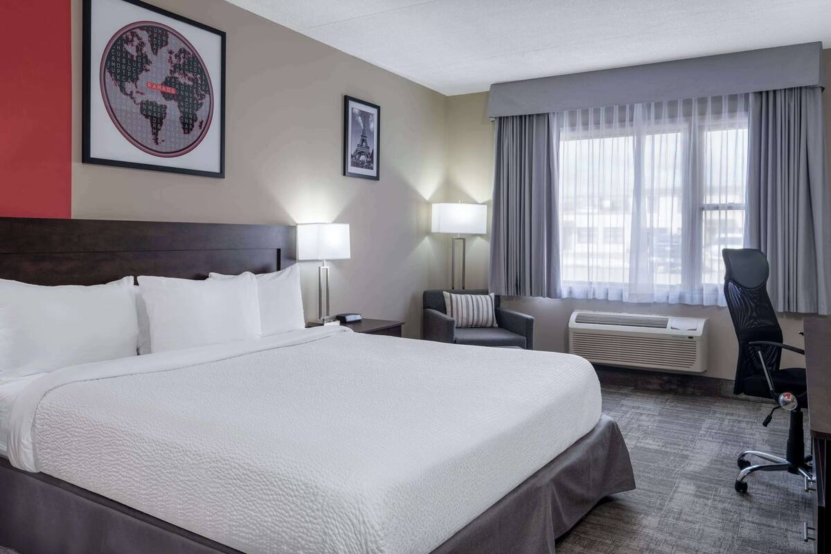 A hotel room with a large bed, a desk, a chair, a lamp, and a world map on the wall.
