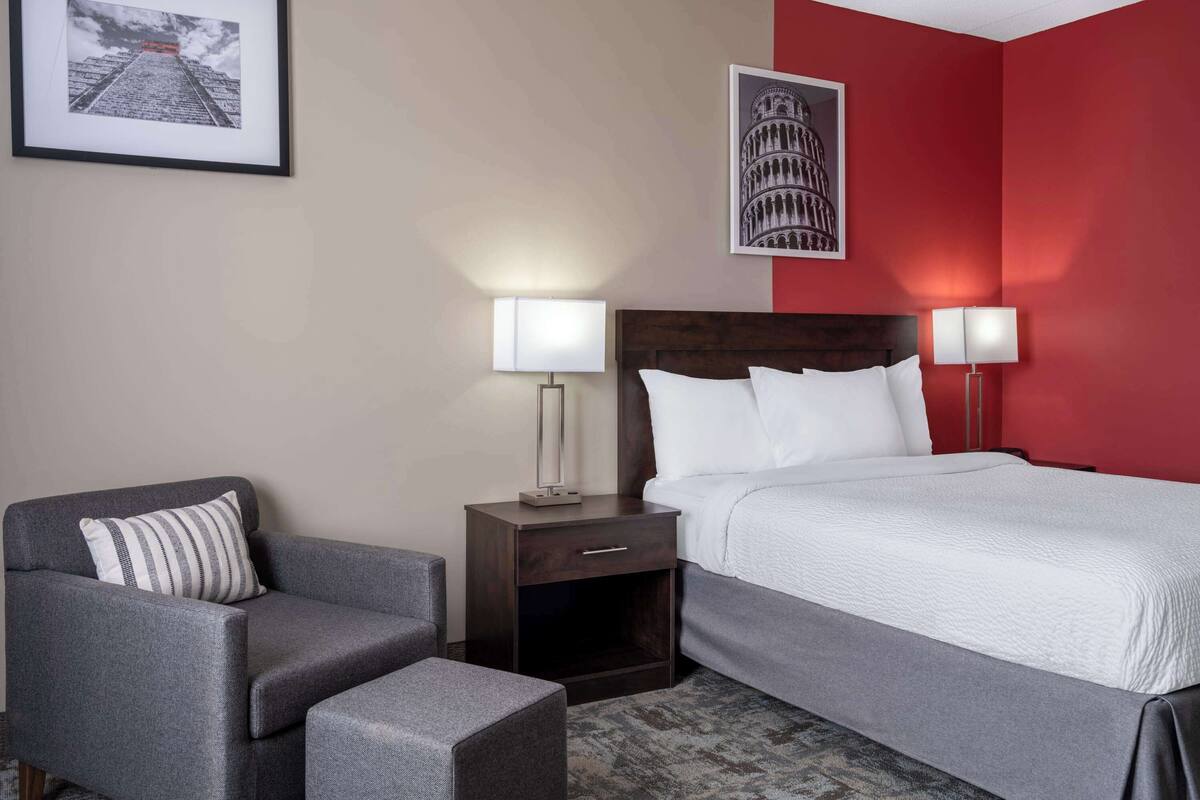 A hotel room with a bed, a nightstand, a chair, and a lamp.