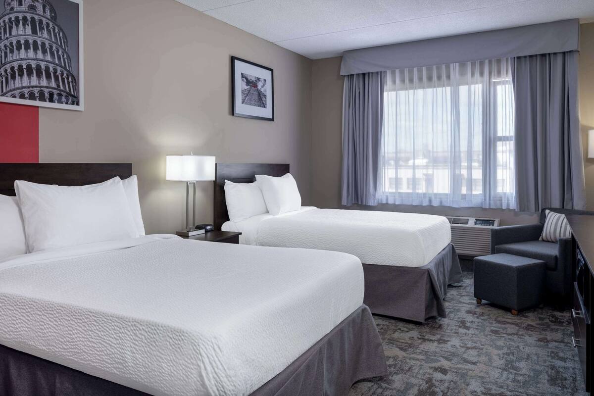 A hotel room with two beds, a desk, a chair, and a window with curtains.