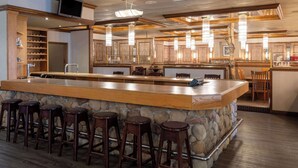 A bar area with a stone counter, wooden stools, and pendant lighting.
