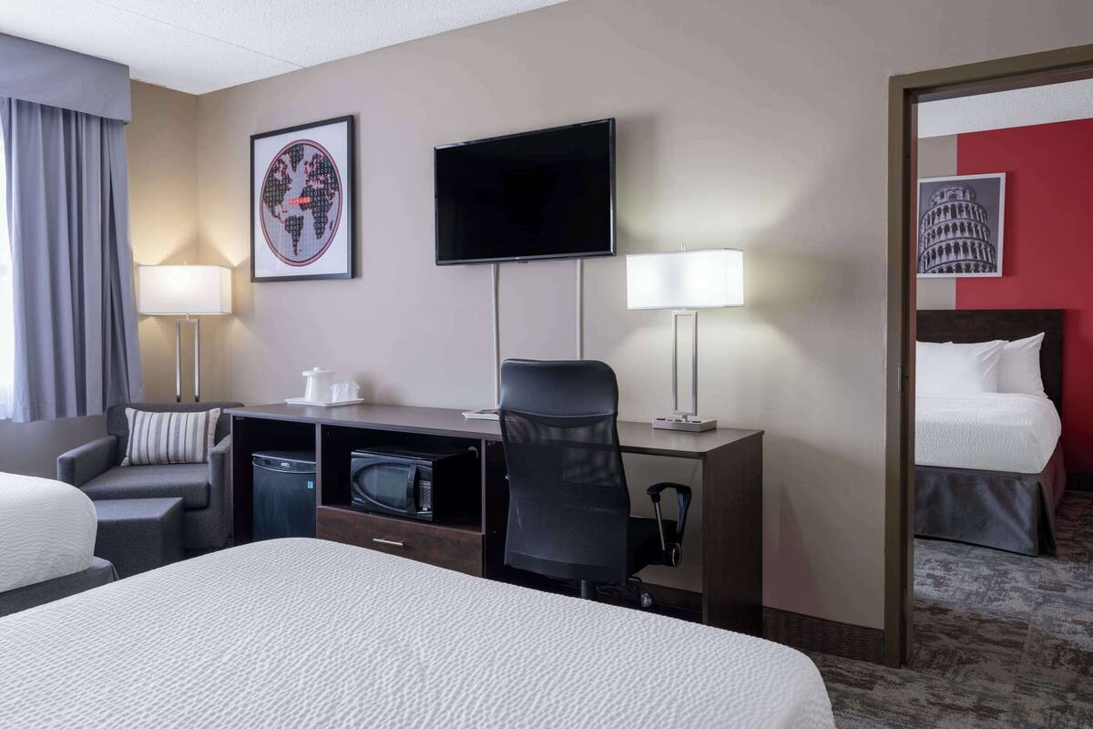 A hotel room with a bed, a desk with a computer, a chair, a TV, and a mirror.