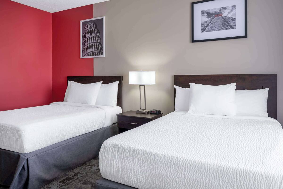 A hotel room with two beds, a nightstand with a lamp, and two framed pictures on the wall.