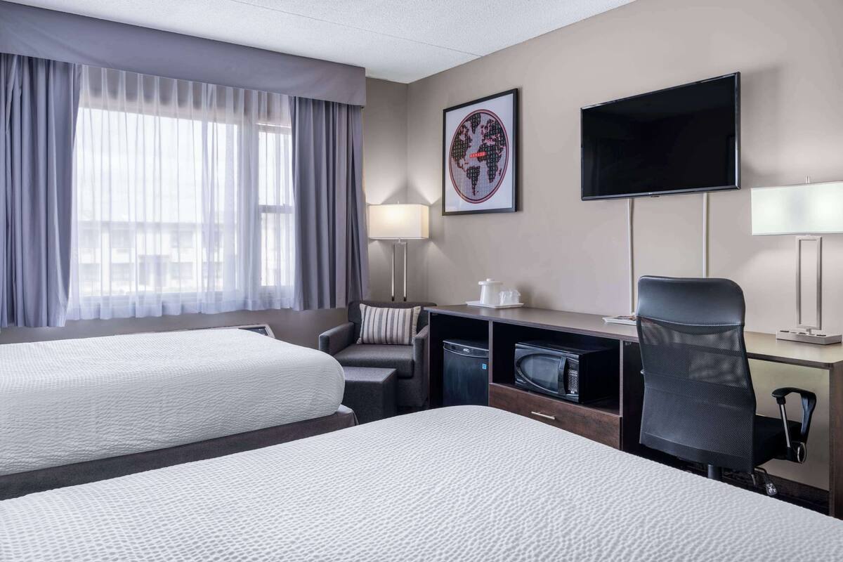 A hotel room with two beds, a desk with a computer, a TV, and a lamp.