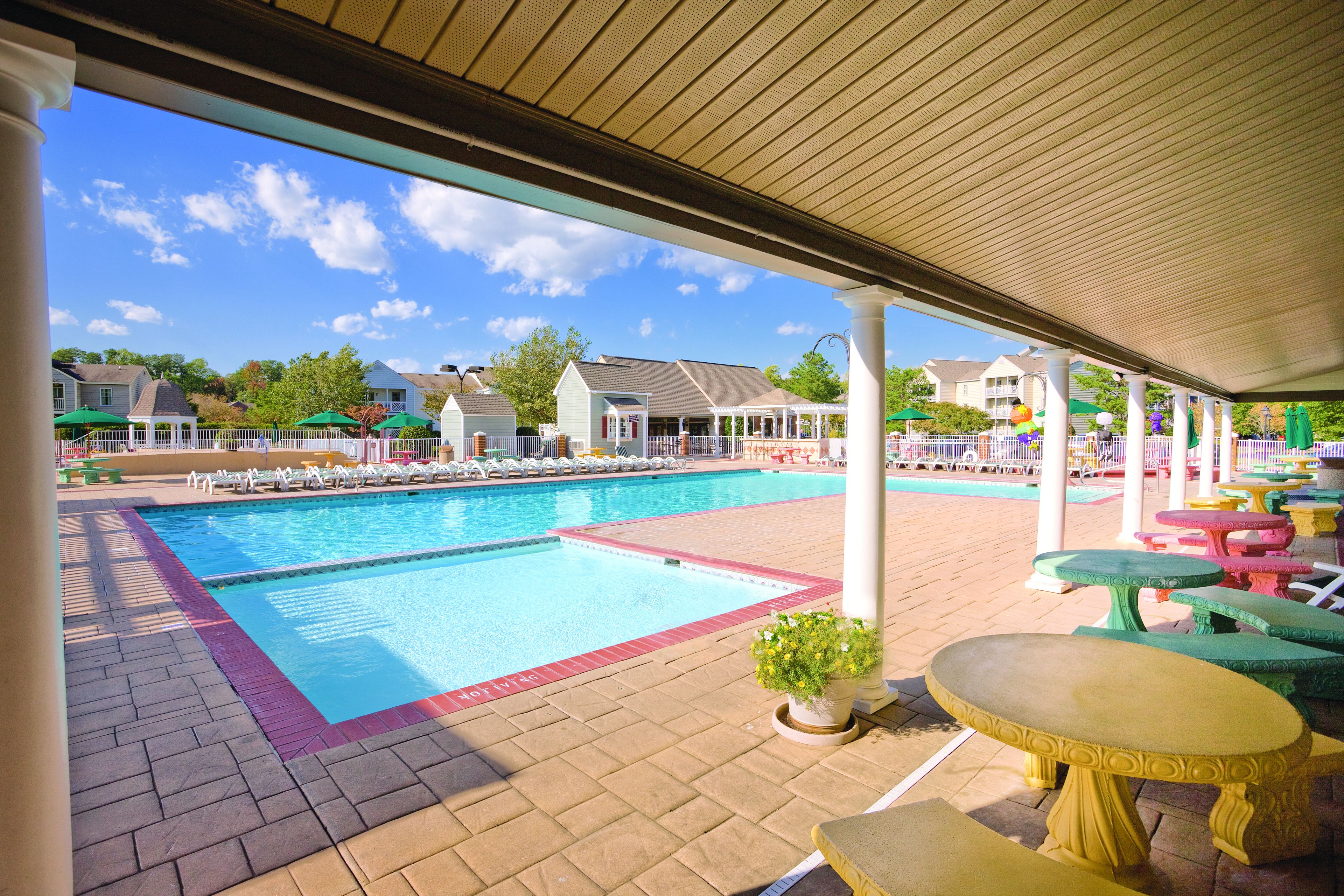 A pool area with a covered patio, lounge chairs, and a pool table.