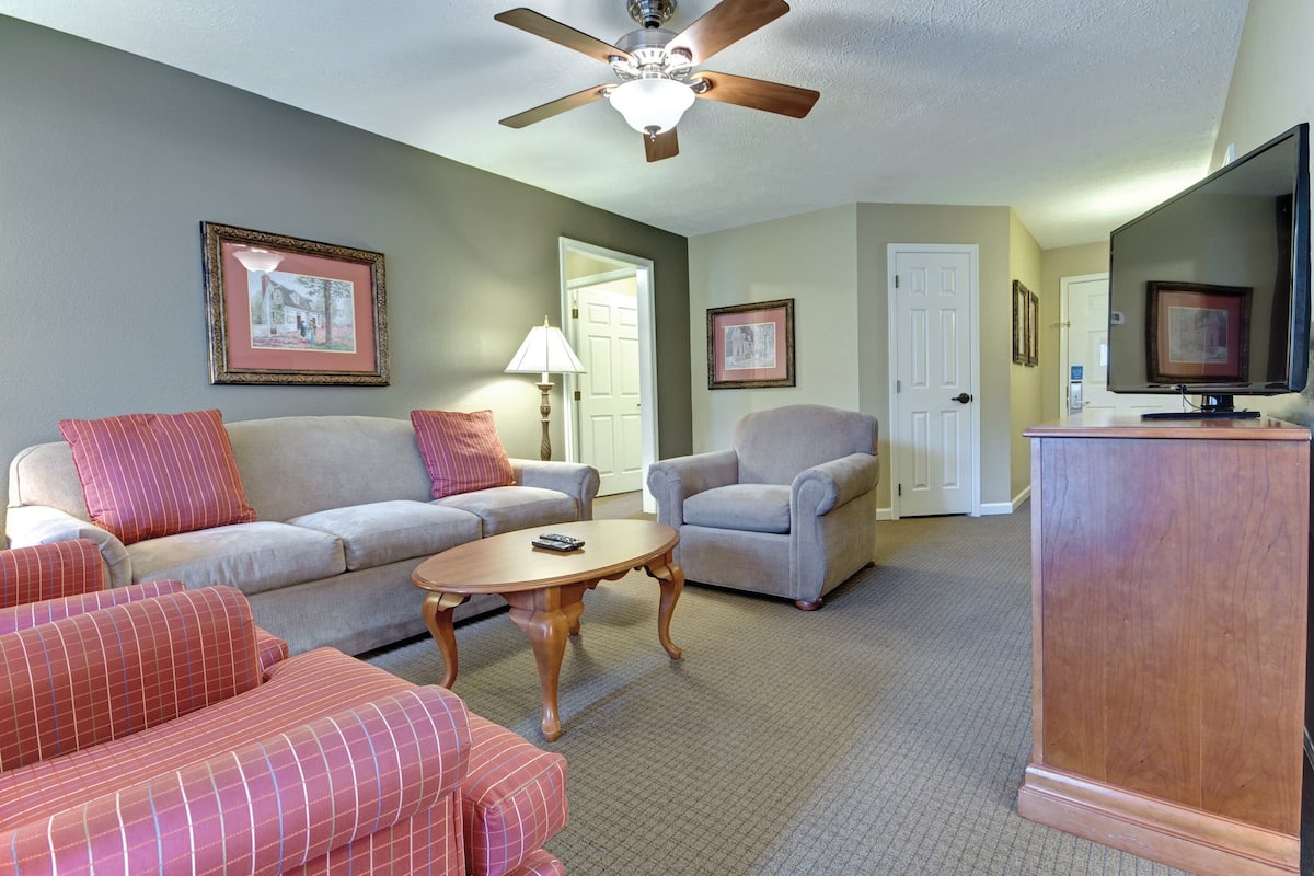 A living room with a ceiling fan, a television, a sofa, a chair, and a small table.