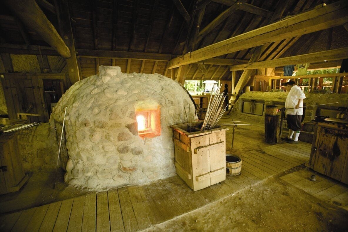 A rustic stone oven with a fire inside, wooden benches, and a rustic interior with wooden beams and a wooden floor.