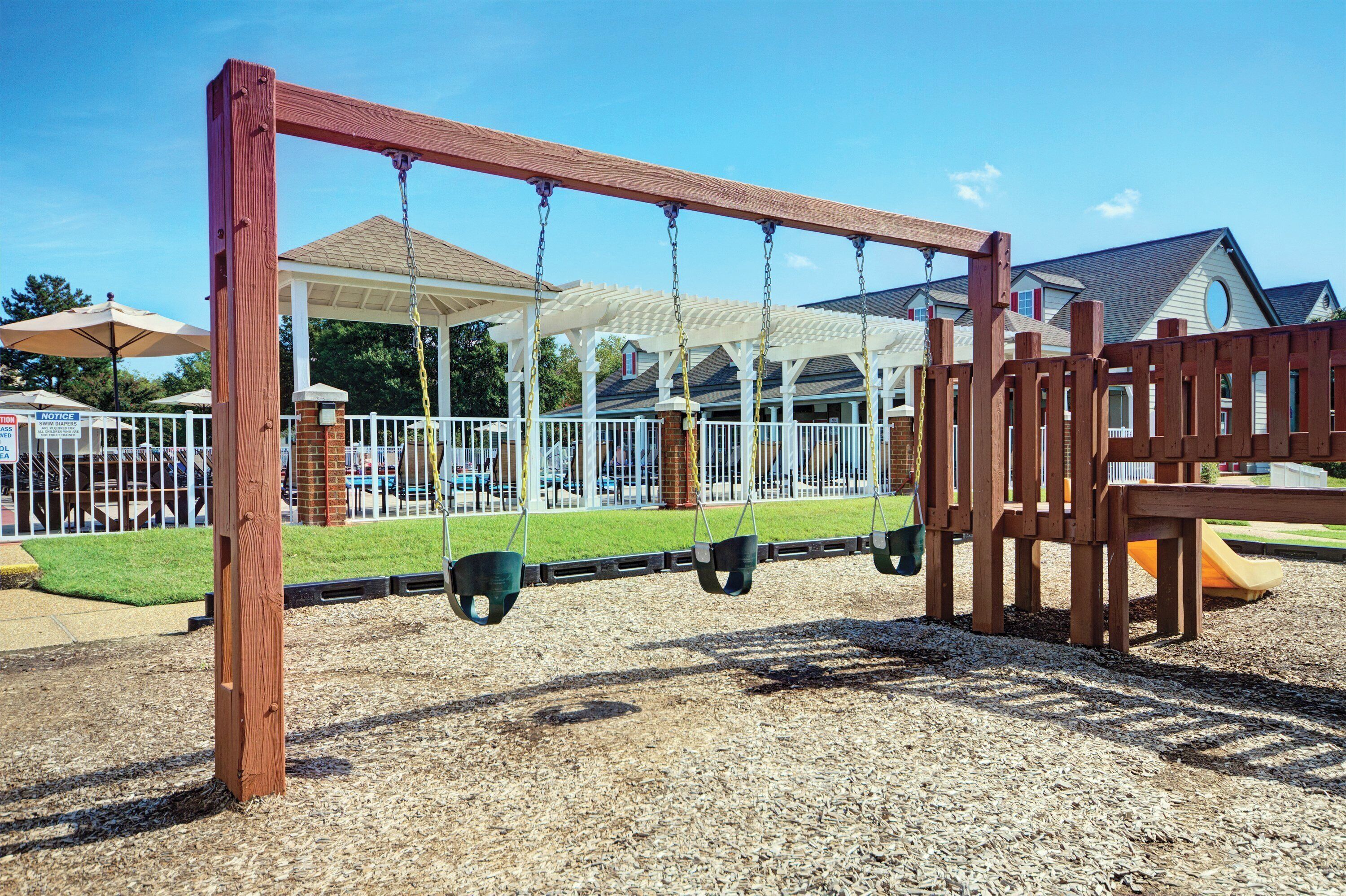 A playground with a swing set, a covered play area, and a fenced play structure.