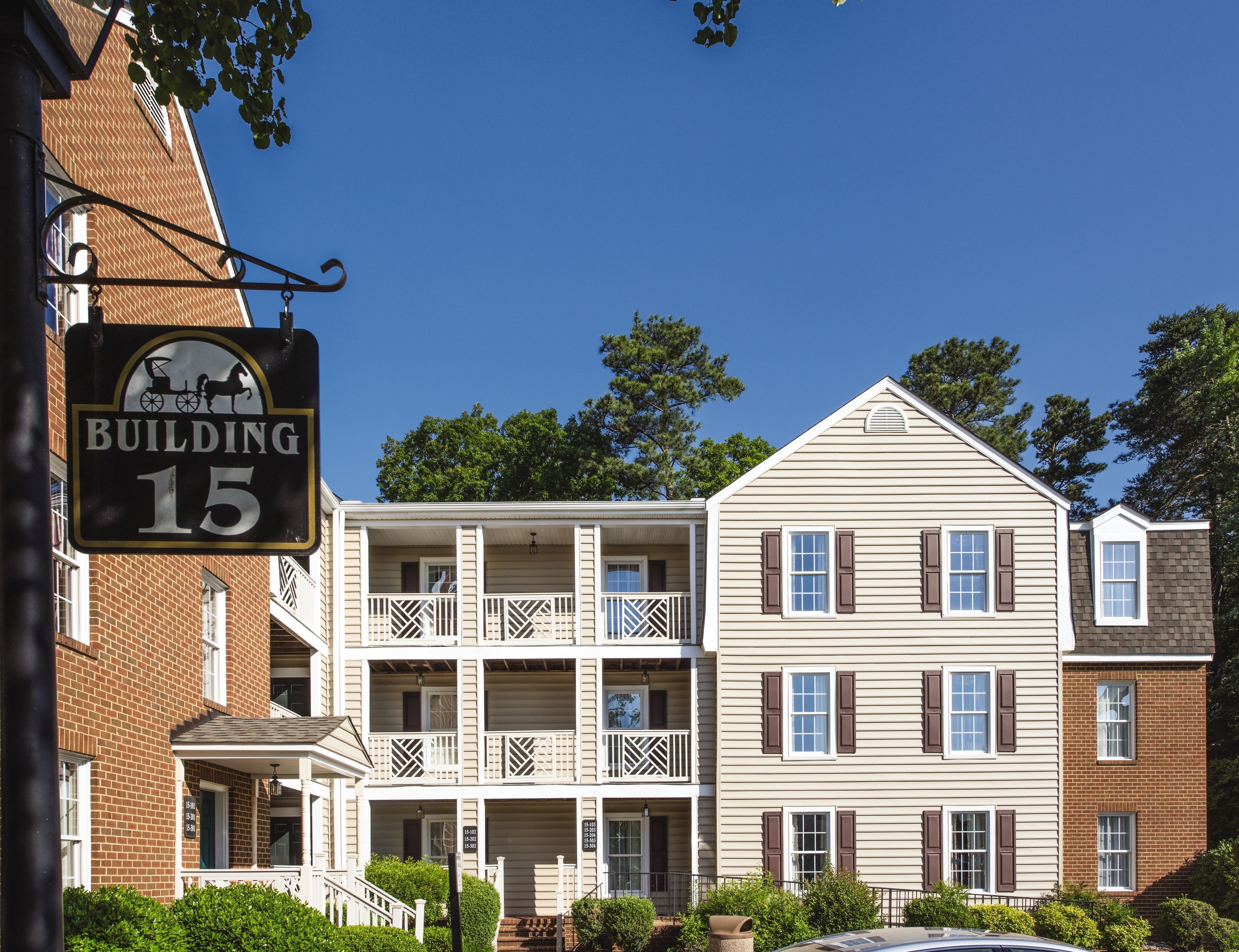 A multi-story building with a sign indicating 'Building 15'. It features a balcony with a lattice railing and a porch with steps leading to the entrance.