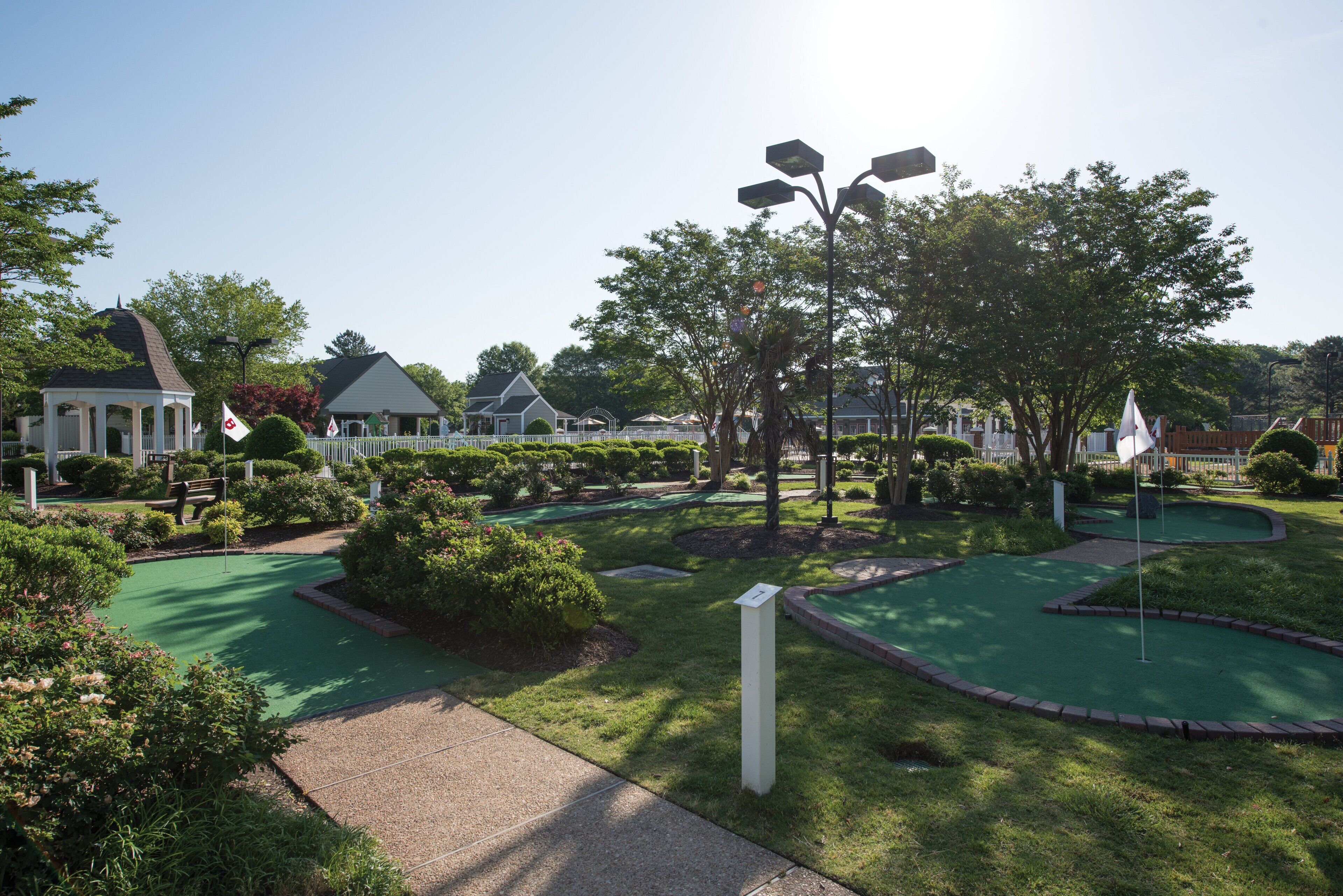 Un campo de mini golf con un pabellón, árboles y cielo despejado.