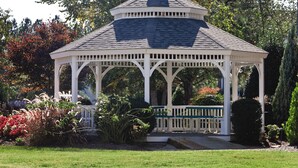 A white gazebo with a peaked roof, surrounded by lush greenery and flowering plants. - Club Wyndham Kingsgate (Williamsburg)