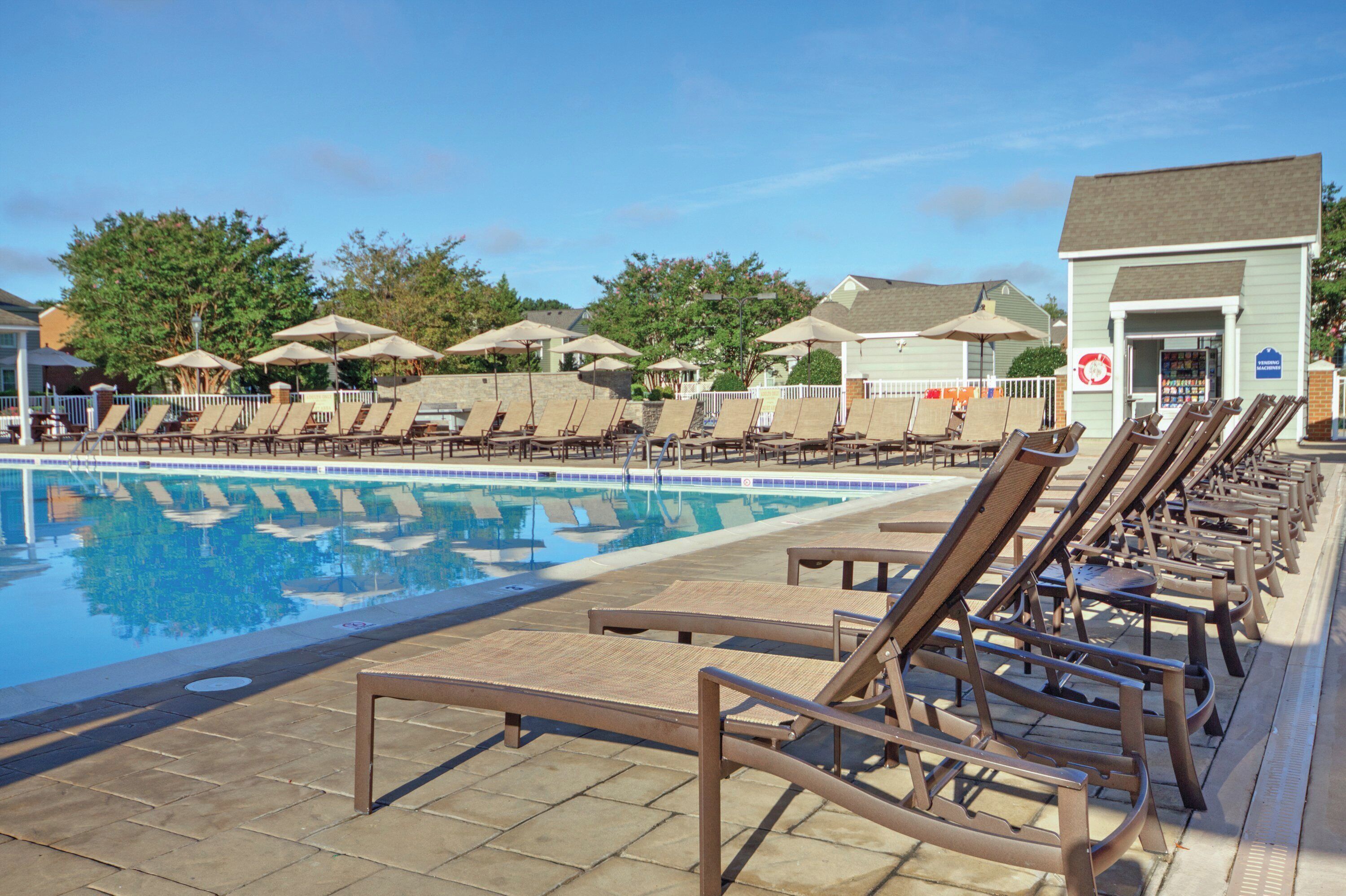 Un espace piscine avec des chaises longues et des parasols, un bâtiment avec une enseigne, et un ciel dégagé.