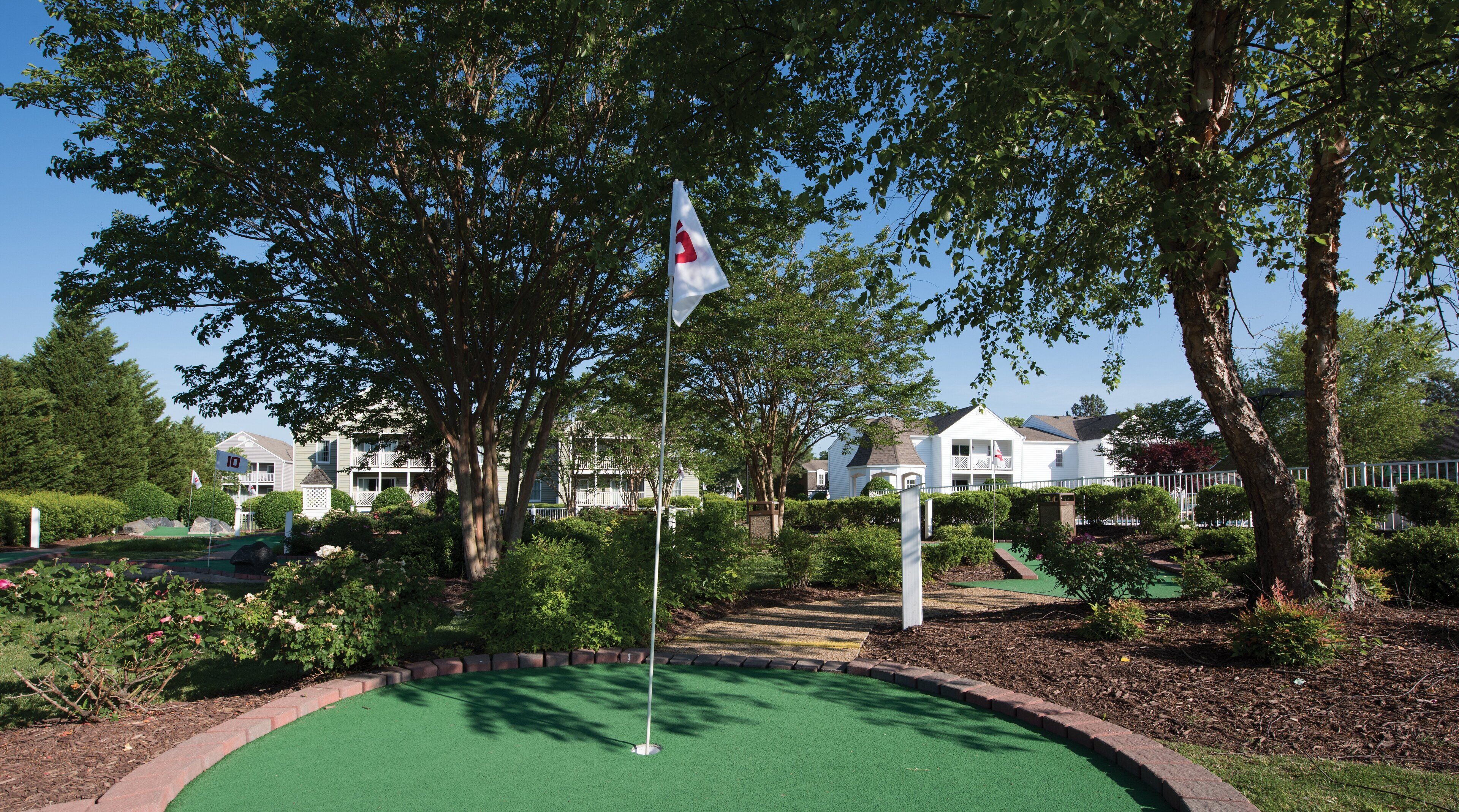 Un terrain de golf avec un mât de drapeau, entouré d’arbres et de maisons d’habitation.