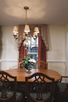 Un comedor con una mesa de madera, seis sillas, una araña y una ventana con cortinas.