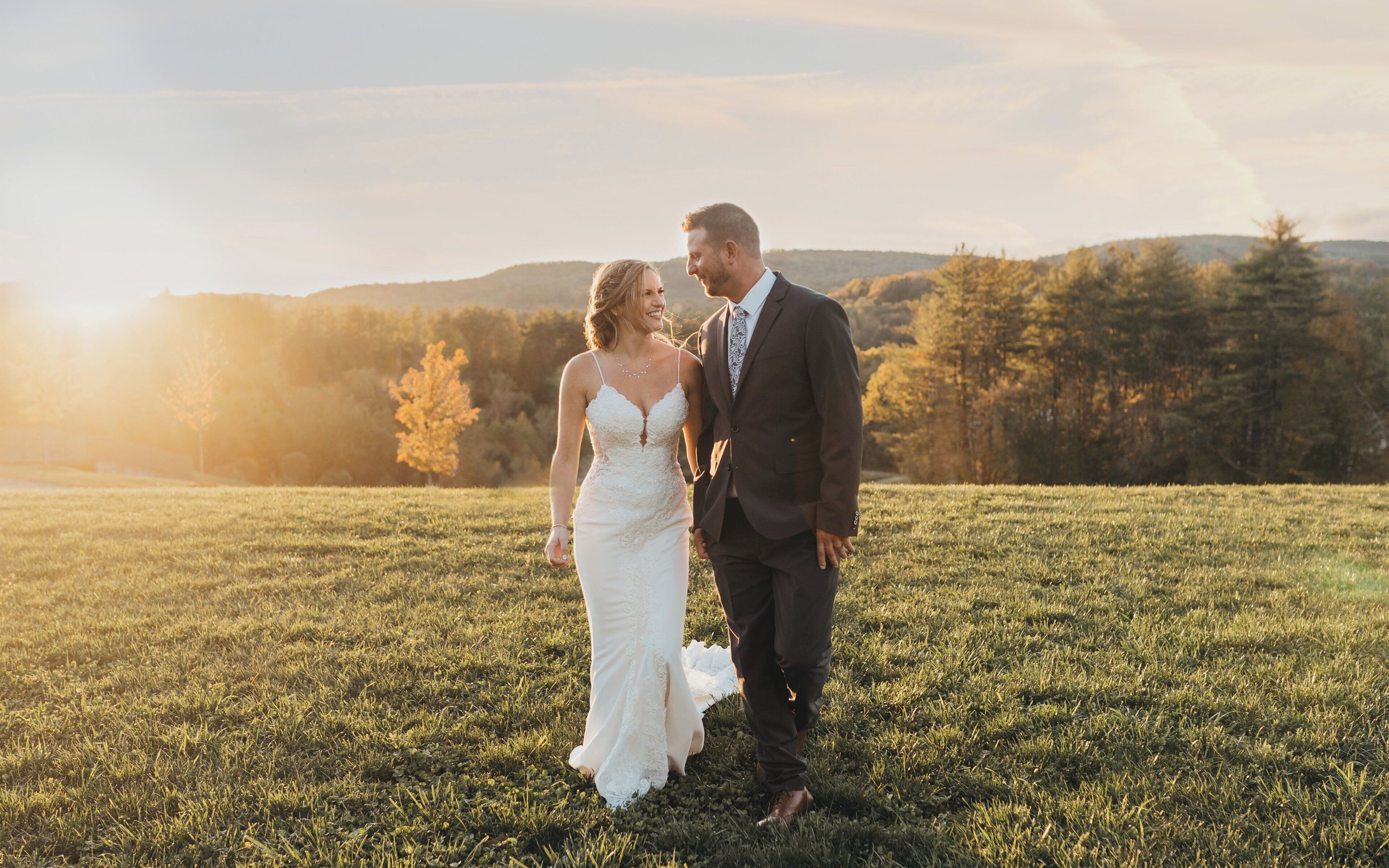 A couple standing in a grassy field with a sunset in the background.