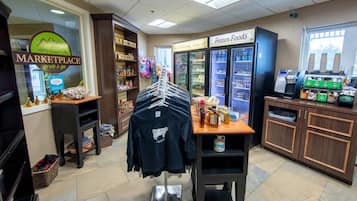 Una tienda con un letrero que dice 'MARKETPLACE', perchas de ropa, un congelador de 'Frozen Foods' y una máquina de café.