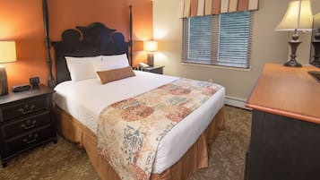 A hotel room with a four-poster bed, bedside tables with lamps, a dresser, and a window with blinds.