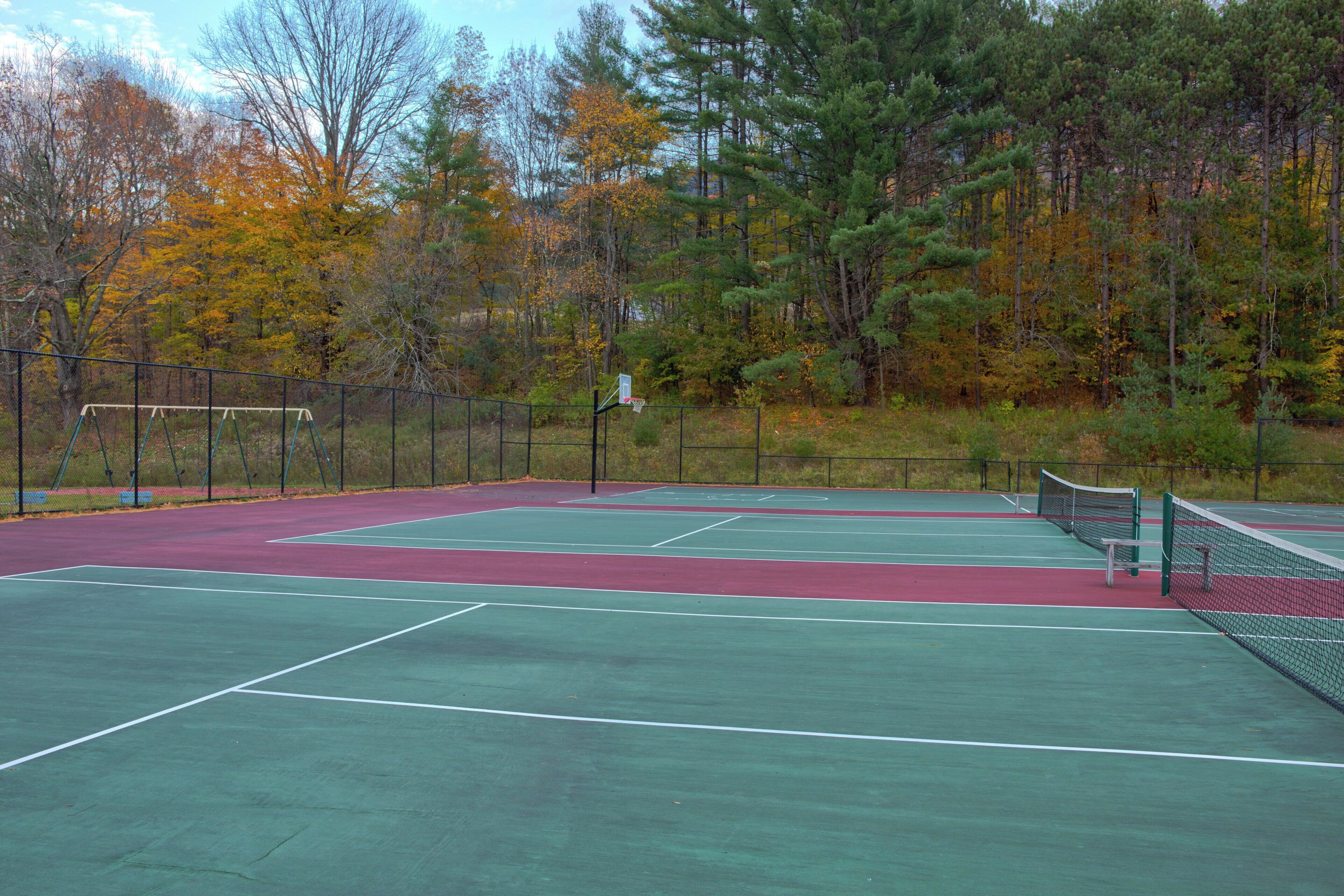 An outdoor tennis court with a net, surrounded by trees and a fence.