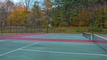 An outdoor tennis court with a net, surrounded by trees and a fence.