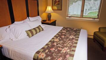 A hotel room with a bed, a nightstand, a lamp, a chair, and a window with blinds.