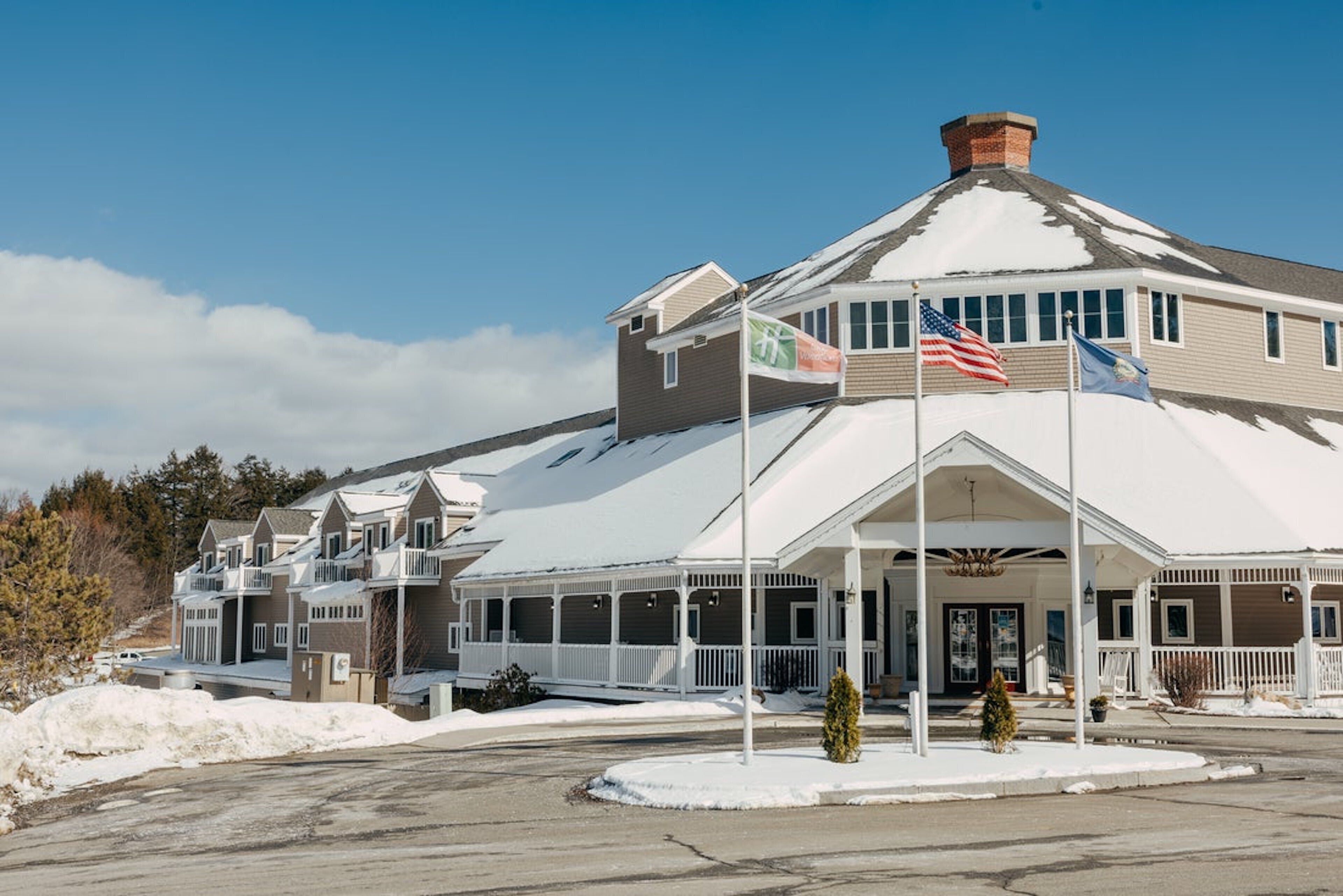 A hotel with a covered entrance, multiple flags, and a snow-covered roof.