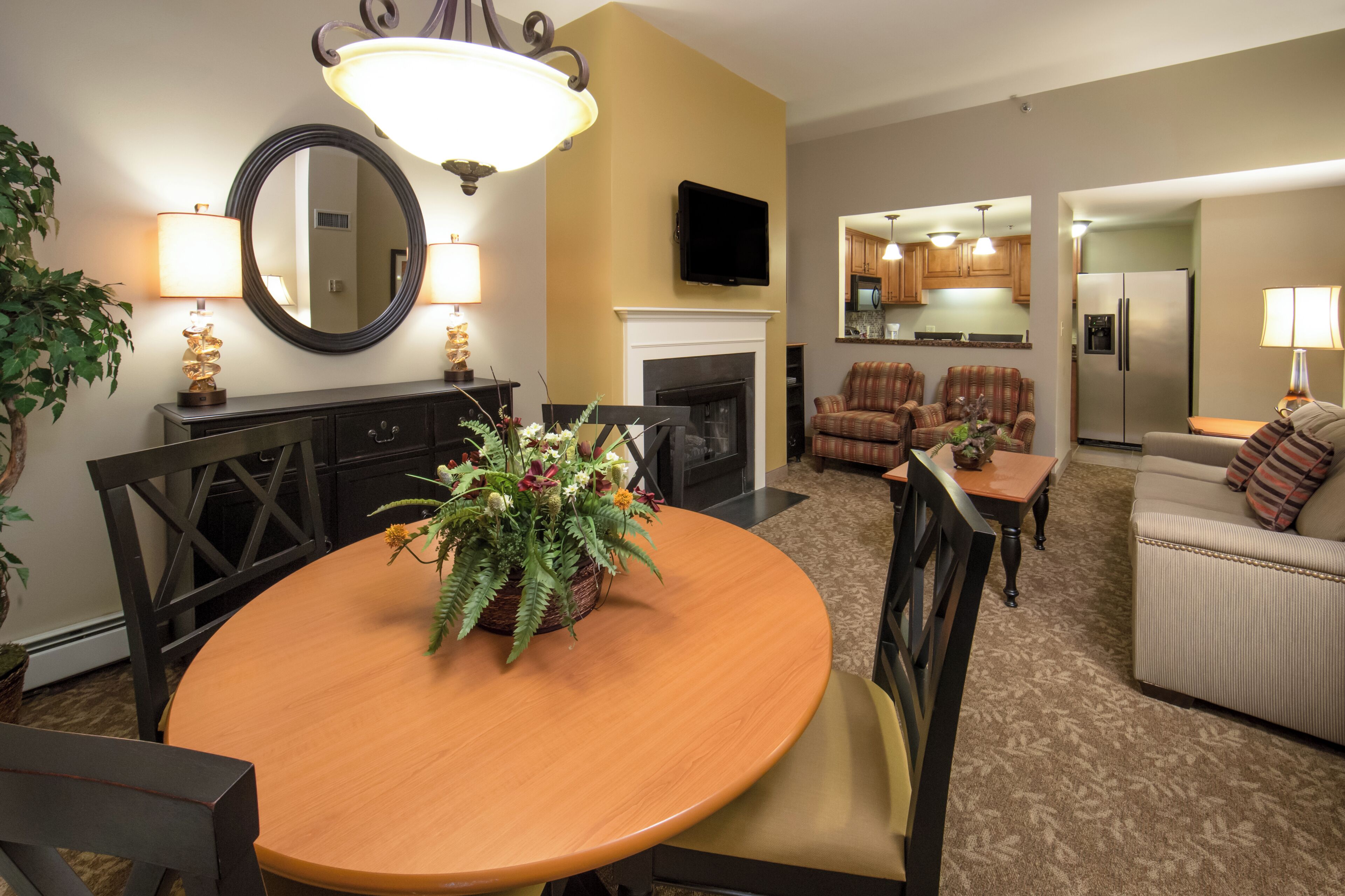 A dining area with a round table, chairs, a mirror, and a fireplace.