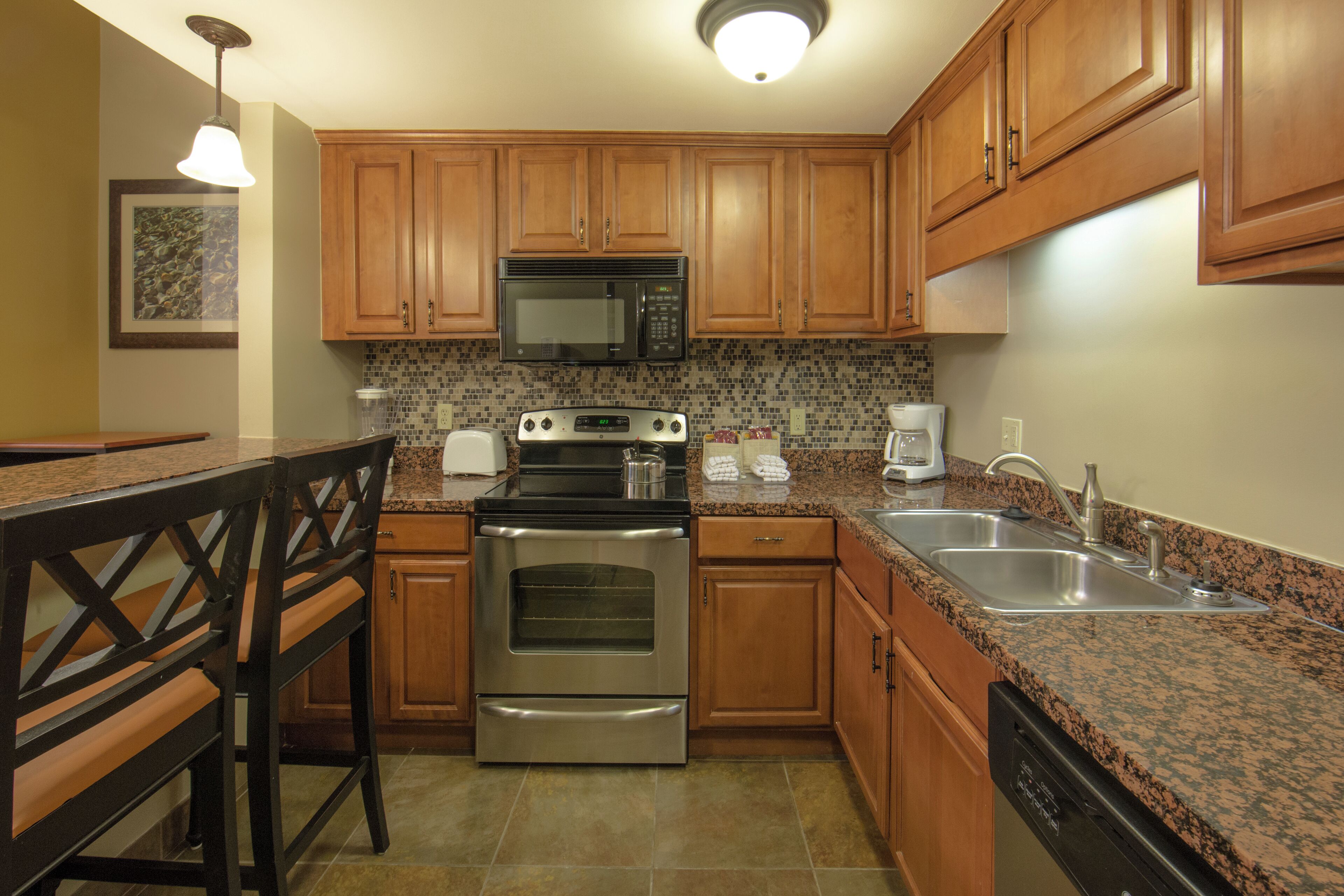 A kitchen with wooden cabinets, a stainless steel oven, a microwave, a granite countertop, and a coffee maker.