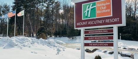 Opastekyltti, jossa on Mount Ascutney Resortin nimi ja Holiday Inn Club Vacations -logon kuva. Kyltti osoittaa, mistä vieraat voivat ilmoittautua ja missä The Maple Kitchen -ravintola sijaitsee.
