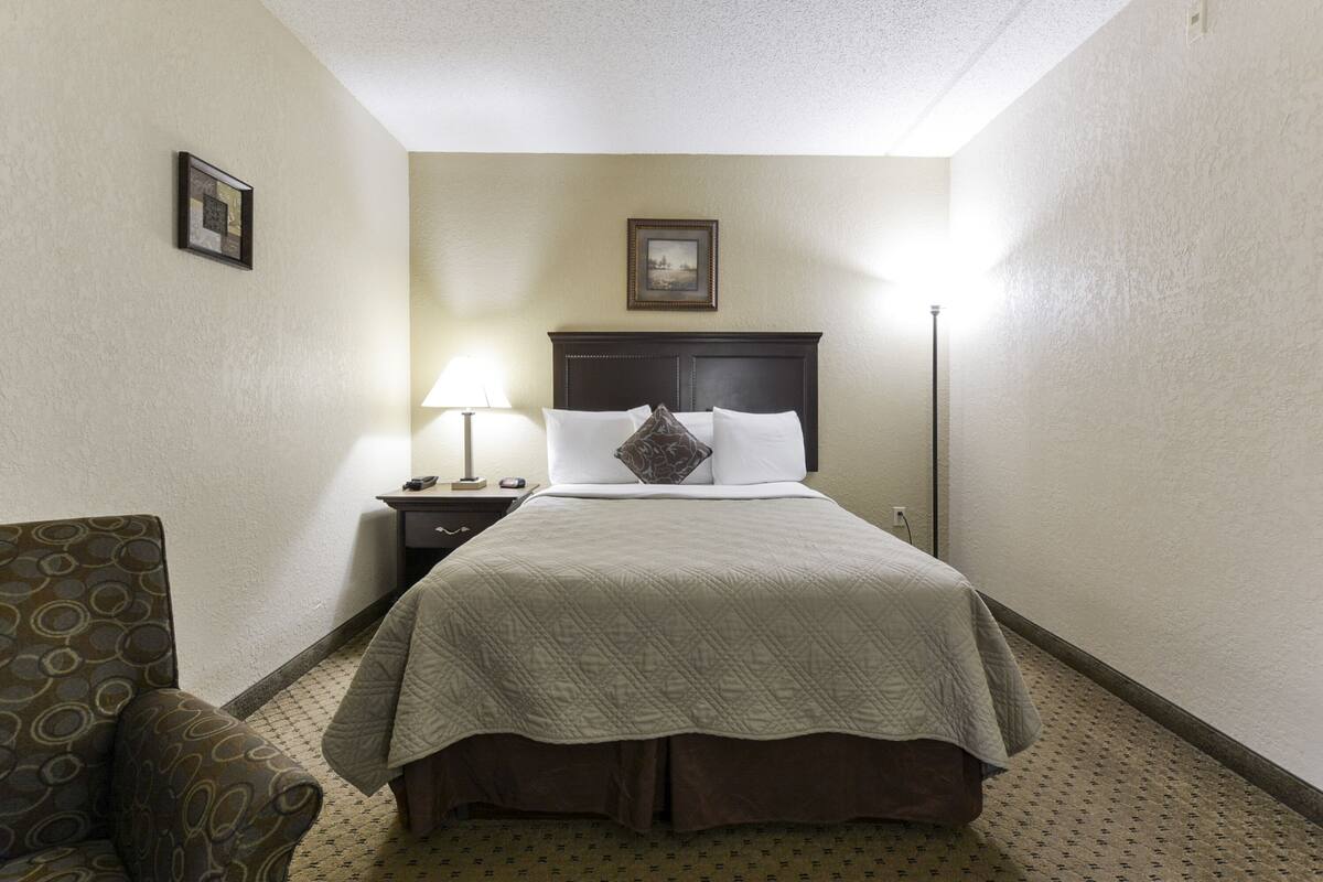 A hotel room with a bed, a nightstand, a lamp, and a chair.