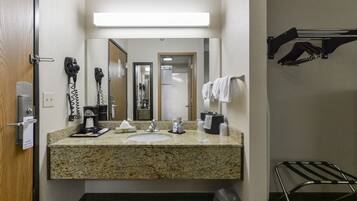 A hotel bathroom with a granite countertop sink, a mirror above it, a hairdryer, a towel rack, and a trash bin.