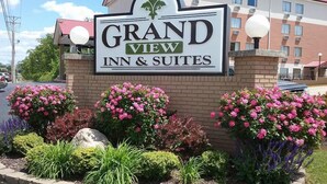 Schild des Grand View Inn & Suites mit Backsteinfassade und Blumenrabatten.