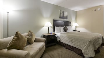 Una habitación de hotel con una cama, dos mesitas de noche con lámparas, un tocador, un sofá y un cuadro en la pared.