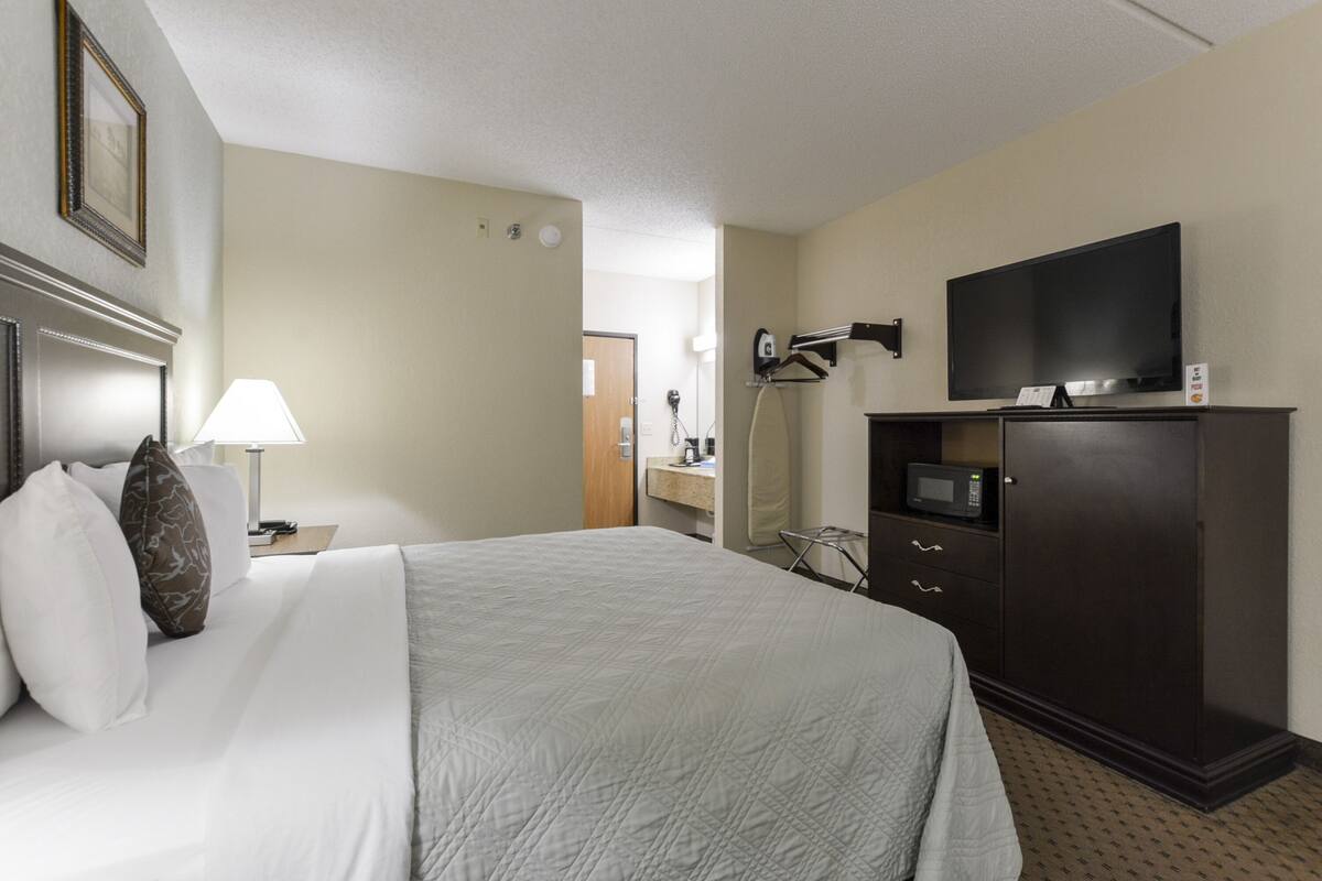 A hotel room with a bed, a TV, a dresser, and a lamp.