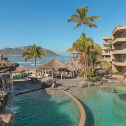 Relax by the oceanfront pool surrounded by palm trees and a natural rock formation with a waterfall.