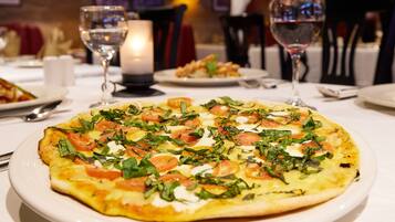 En pizza med tomater og basilikum på en hvid tallerken.