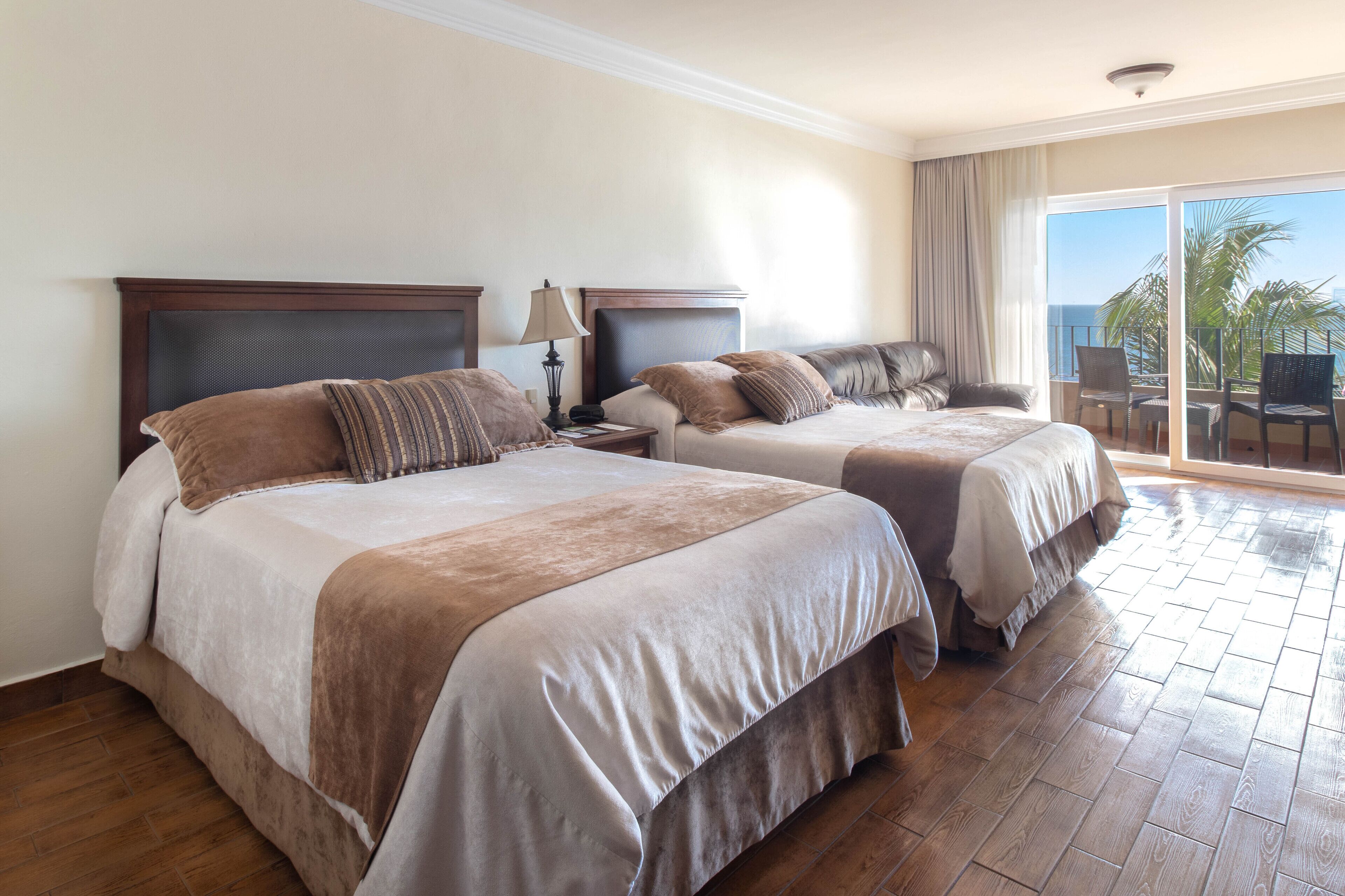 A hotel room with two beds, a balcony with a view, and a wooden floor.