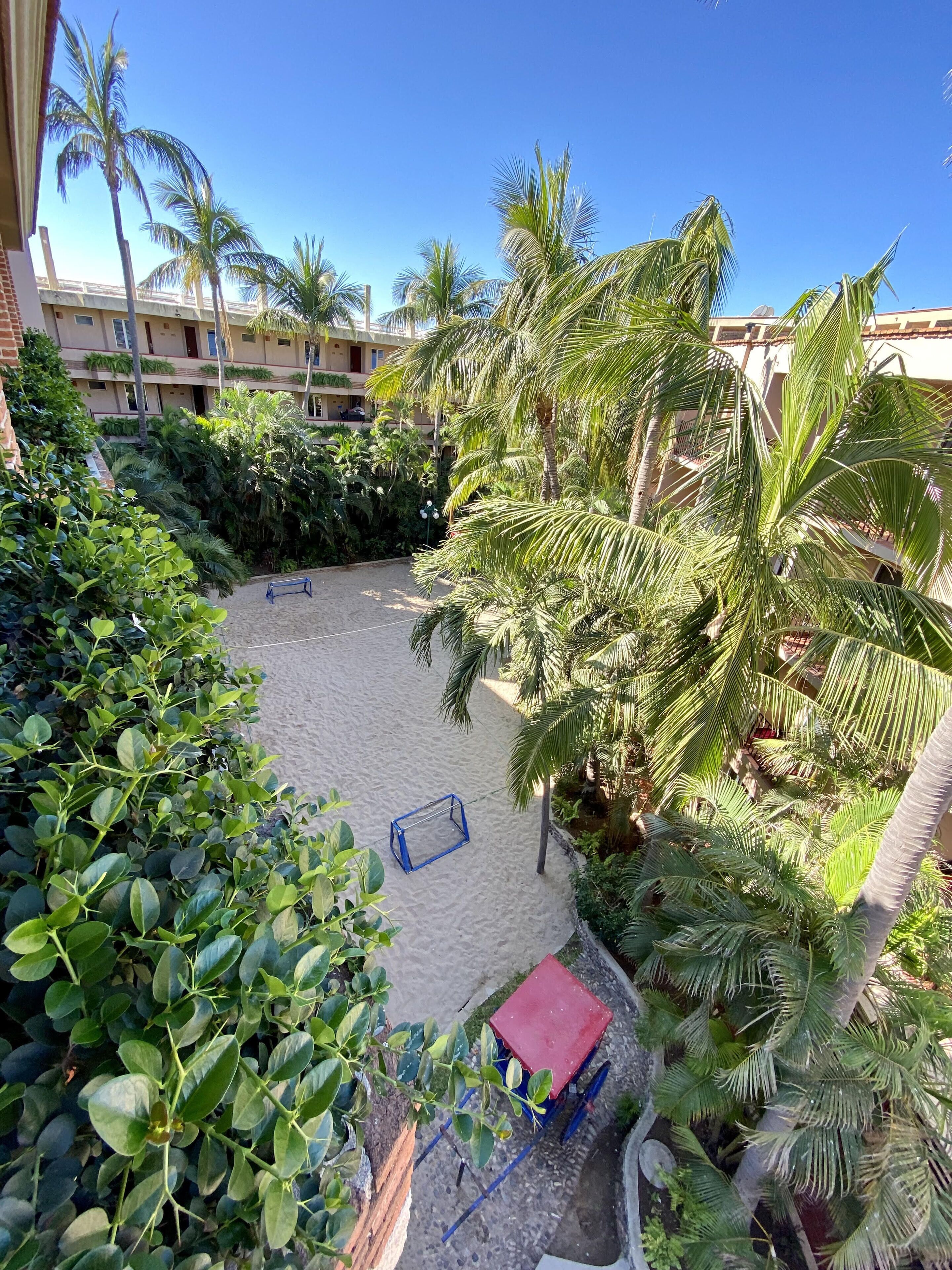 A courtyard with a sandy play area, surrounded by lush greenery and palm trees.